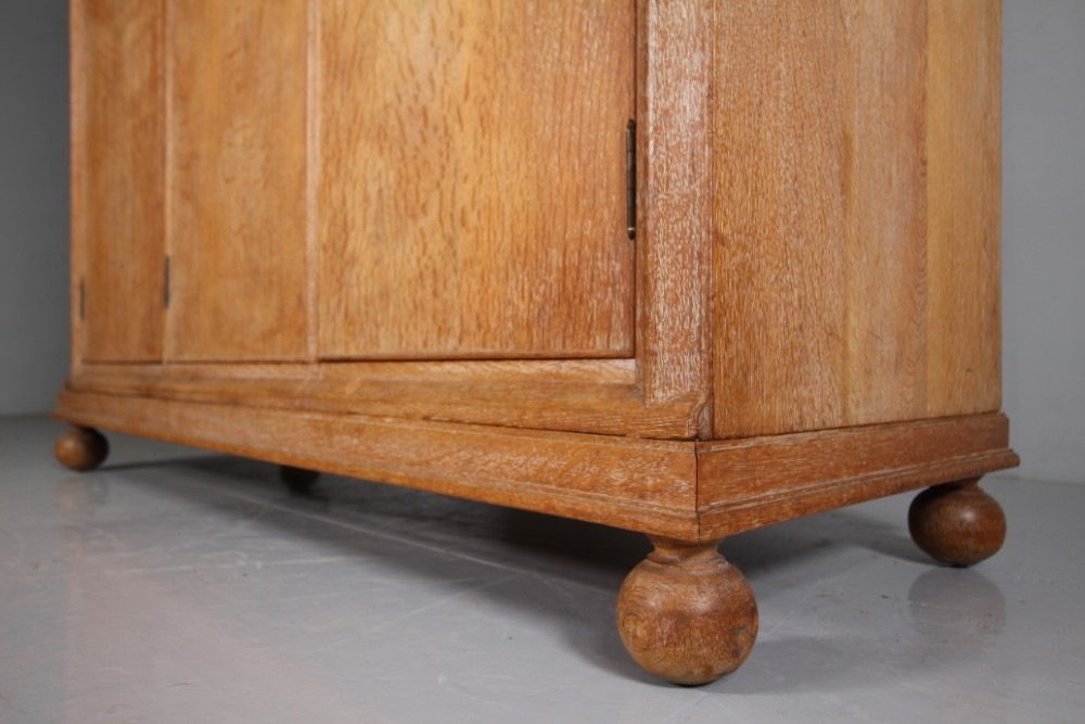 A 1920s Heals solid oak triple-door wardrobe with chamfered top corners, vertical wooden handles, and bun feet. View VI