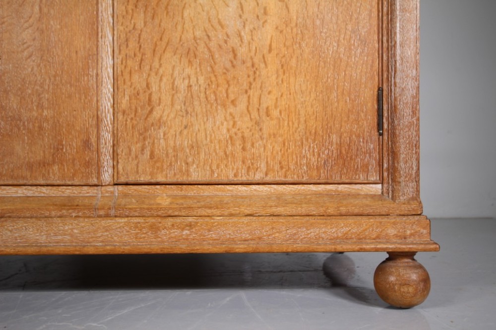 A 1920s Heals solid oak triple-door wardrobe with chamfered top corners, vertical wooden handles, and bun feet. View IX