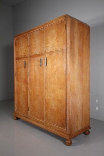 A 1920s Heals solid oak triple-door wardrobe with chamfered top corners, vertical wooden handles, and bun feet. View V