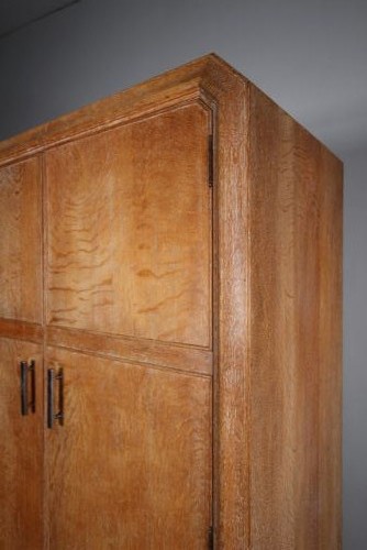 A 1920s Heals solid oak triple-door wardrobe with chamfered top corners, vertical wooden handles, and bun feet. View VII