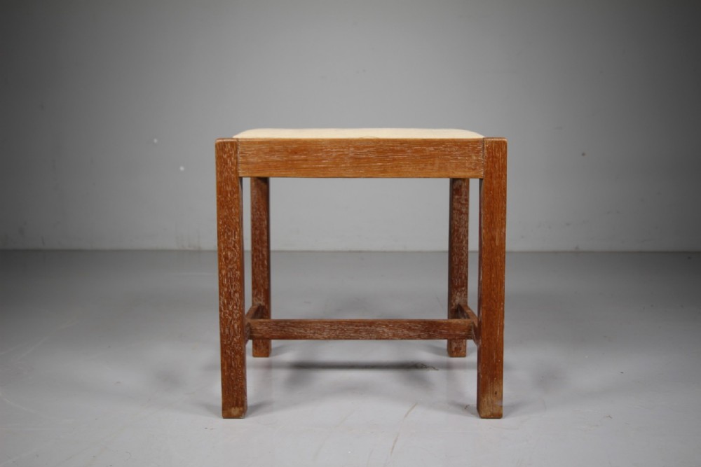 A 1920s oak stool featuring square straight legs connected by low stretchers and topped with a cushioned off-white seat. View II