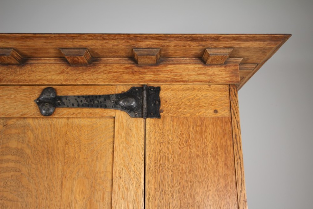 An Arts and Crafts solid oak cupboard featuring hand-forged wrought iron strap hinges, a single panelled door, and a lower drawer. View V