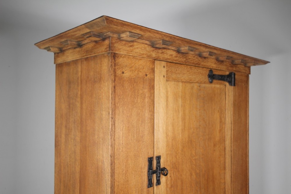 An Arts and Crafts solid oak cupboard featuring hand-forged wrought iron strap hinges, a single panelled door, and a lower drawer. View IX