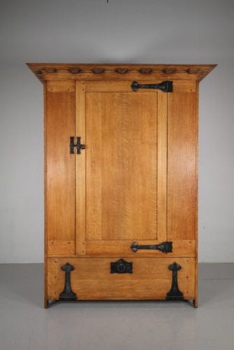 An Arts and Crafts solid oak cupboard featuring hand-forged wrought iron strap hinges, a single panelled door, and a lower drawer. View II