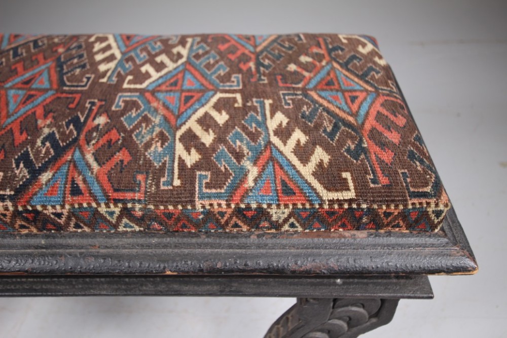 An early nineteenth-century black painted pine window seat featuring carved scroll legs decorated with repeating motifs and an upholstered geometric pad. View V