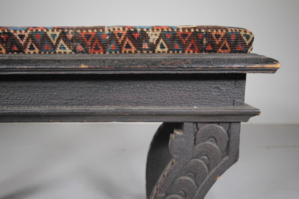 An early nineteenth-century black painted pine window seat featuring carved scroll legs decorated with repeating motifs and an upholstered geometric pad. View VI