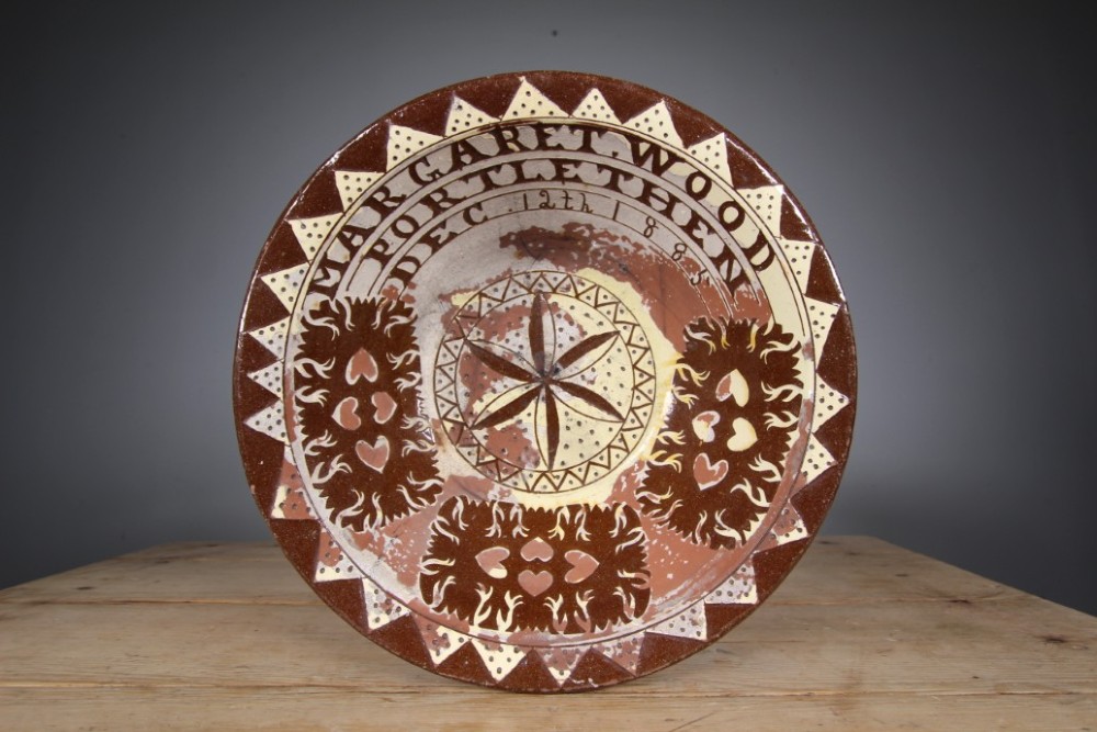 A large circular 19th-century slipware earthenware bowl decorated with cream geometric patterns, heart motifs, a central rosette, and inscribed text reading Margaret Wood Portlethen Dec 12th 1883.