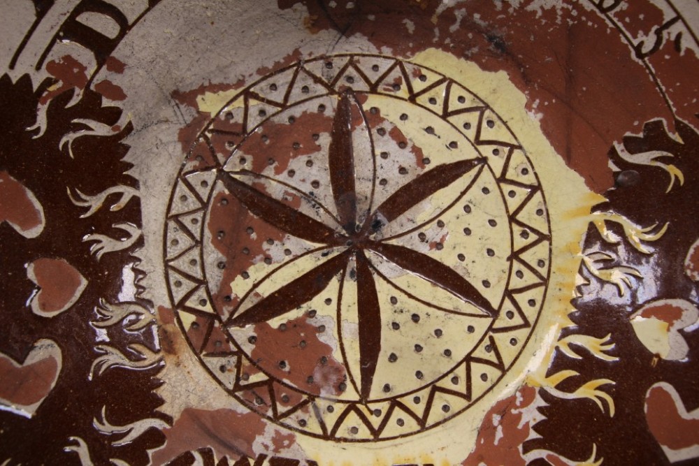 A large circular 19th-century slipware earthenware bowl decorated with cream geometric patterns, heart motifs, a central rosette, and inscribed text reading Margaret Wood Portlethen Dec 12th 1883. View IV