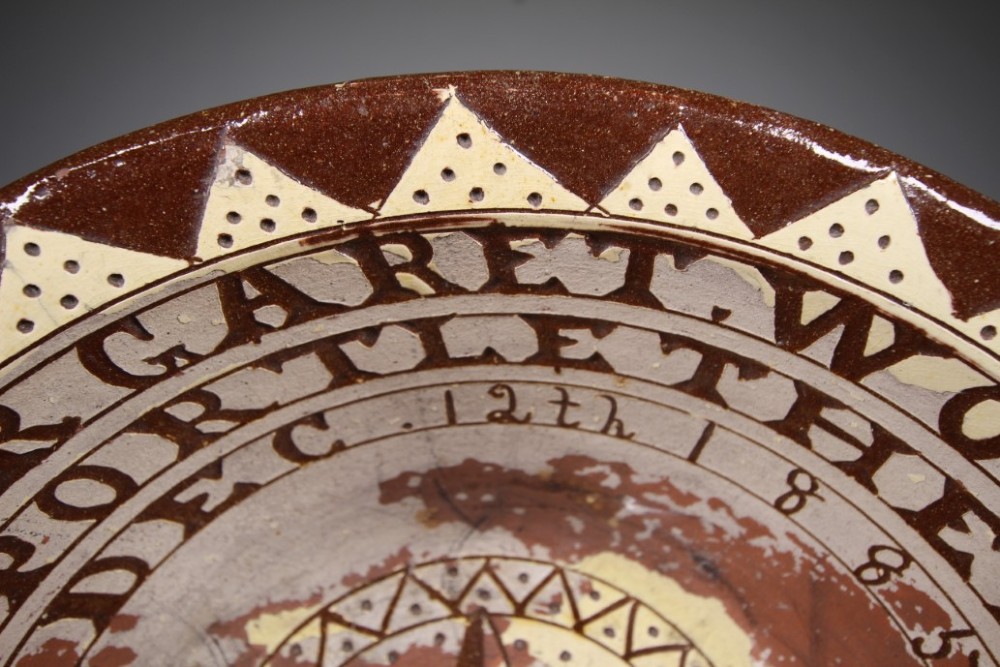 A large circular 19th-century slipware earthenware bowl decorated with cream geometric patterns, heart motifs, a central rosette, and inscribed text reading Margaret Wood Portlethen Dec 12th 1883. View V