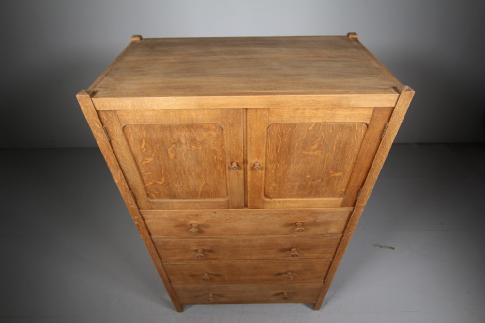 A 1920s Heals oak tallboy cupboard with two panelled upper doors above four wide graduated drawers fitted with circular wooden knobs. View II