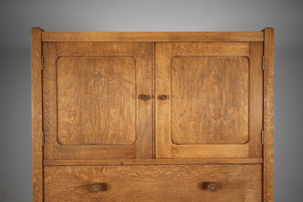 A 1920s Heals oak tallboy cupboard with two panelled upper doors above four wide graduated drawers fitted with circular wooden knobs. View IV