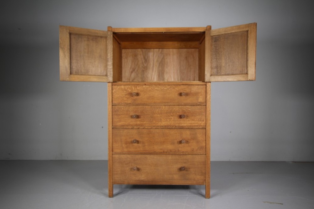 A 1920s Heals oak tallboy cupboard with two panelled upper doors above four wide graduated drawers fitted with circular wooden knobs. View VI
