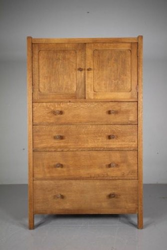 A 1920s Heals oak tallboy cupboard with two panelled upper doors above four wide graduated drawers fitted with circular wooden knobs.