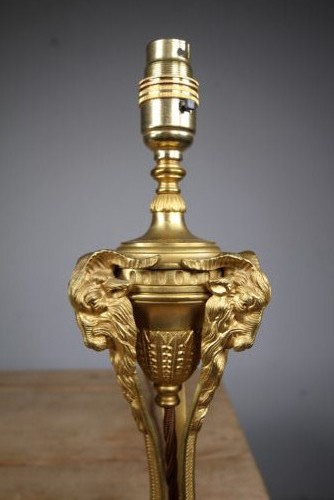 A 19th-century Neoclassical gilt bronze table lamp featuring a central urn, tri-form tripod legs terminating in rams heads, and a raised socket. View V