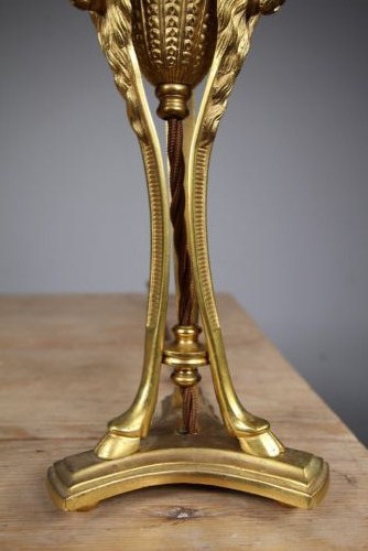 A 19th-century Neoclassical gilt bronze table lamp featuring a central urn, tri-form tripod legs terminating in rams heads, and a raised socket. View VI