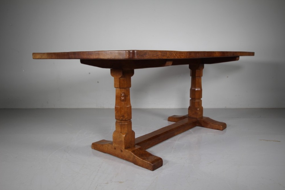 An English Arts and Crafts adzed oak refectory dining table featuring octagonal pedestal legs connected by a floor stretcher, displaying a carved mouse signature.