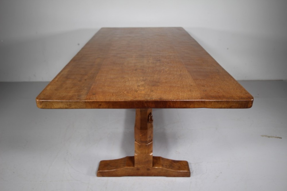 An English Arts and Crafts adzed oak refectory dining table featuring octagonal pedestal legs connected by a floor stretcher, displaying a carved mouse signature. View III