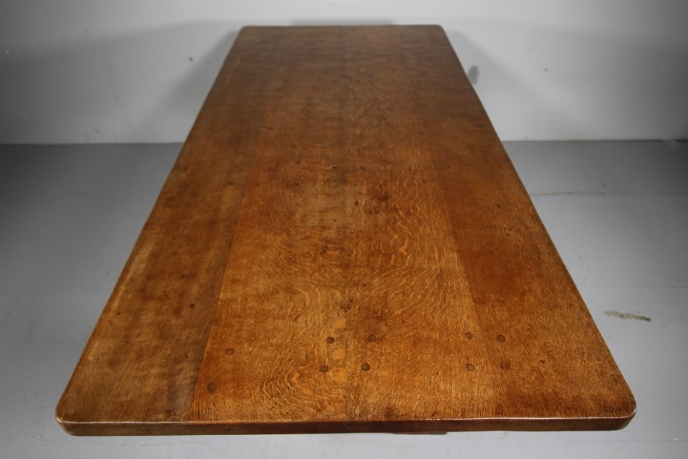 An English Arts and Crafts adzed oak refectory dining table featuring octagonal pedestal legs connected by a floor stretcher, displaying a carved mouse signature. View IV