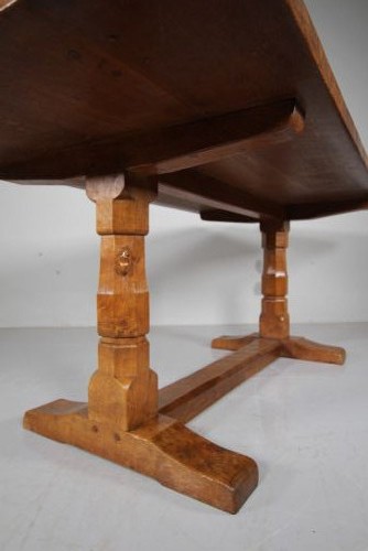 An English Arts and Crafts adzed oak refectory dining table featuring octagonal pedestal legs connected by a floor stretcher, displaying a carved mouse signature. View X