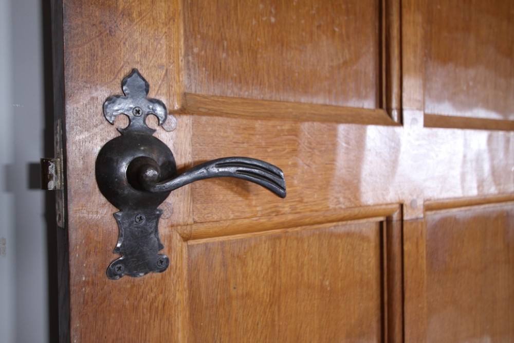 A solid oak interior door featuring ten raised panels, a hand-adzed textured finish, wrought iron latch hardware, and a carved mouse detail. View XII