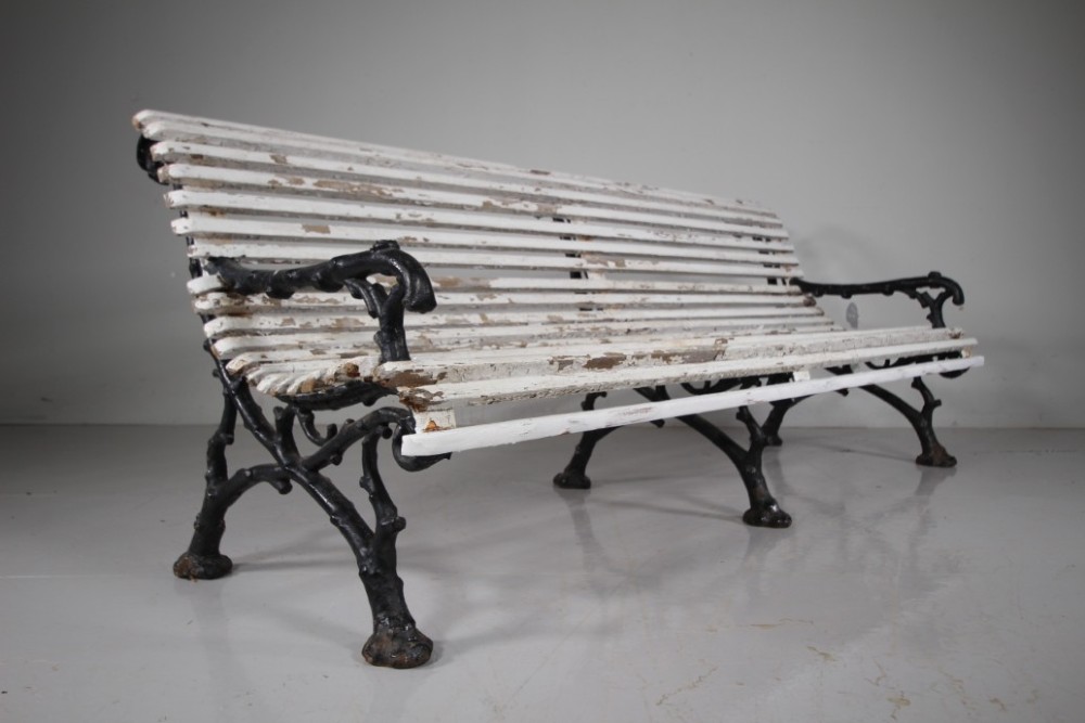 A 19th-century garden bench featuring black cast iron frame ends moulded in a branch pattern with weathered white painted wooden slats forming the backrest and seat.