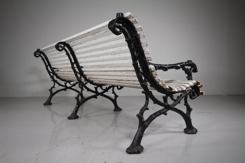 A 19th-century garden bench featuring black cast iron frame ends moulded in a branch pattern with weathered white painted wooden slats forming the backrest and seat. View II