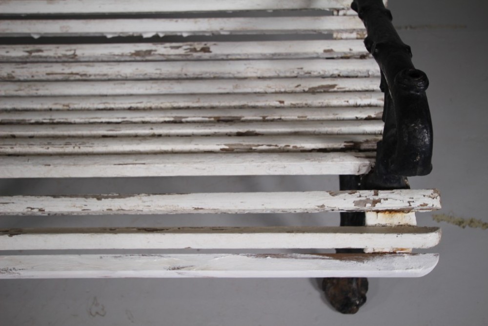 A 19th-century garden bench featuring black cast iron frame ends moulded in a branch pattern with weathered white painted wooden slats forming the backrest and seat. View V