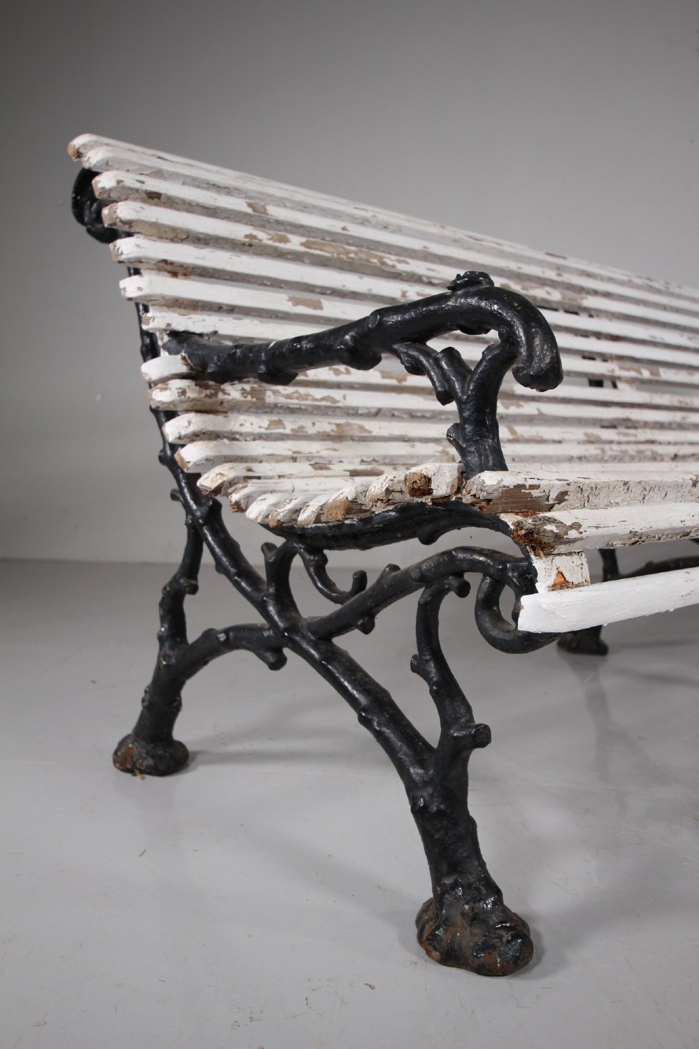 A 19th-century garden bench featuring black cast iron frame ends moulded in a branch pattern with weathered white painted wooden slats forming the backrest and seat. View VII