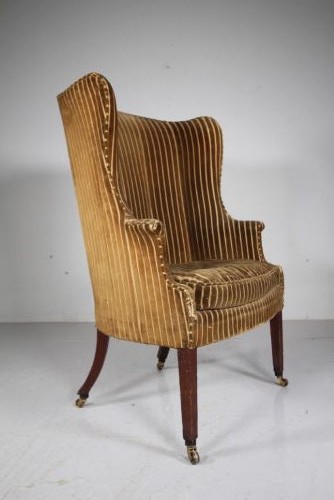 A Georgian style high back barrel armchair upholstered in striped gold velvet, featuring square tapered mahogany front legs on brass castors. View III
