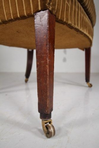 A Georgian style high back barrel armchair upholstered in striped gold velvet, featuring square tapered mahogany front legs on brass castors. View IV