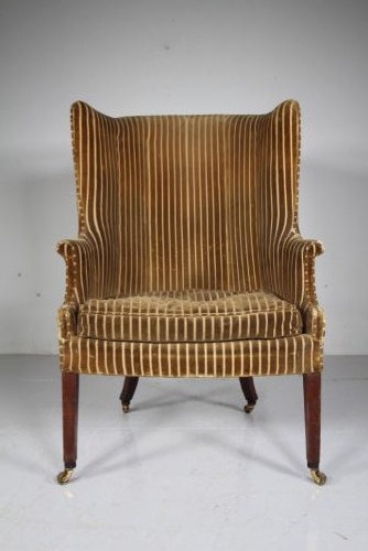 A Georgian style high back barrel armchair upholstered in striped gold velvet, featuring square tapered mahogany front legs on brass castors. View VII