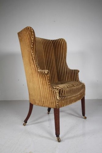 A Georgian style high back barrel armchair upholstered in striped gold velvet, featuring square tapered mahogany front legs on brass castors.