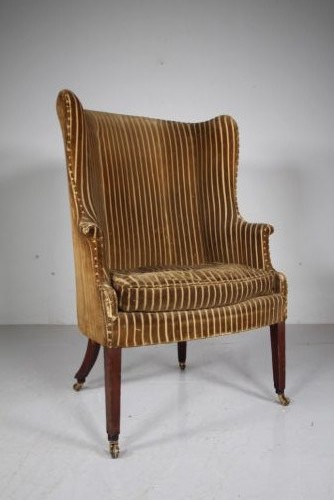 A Georgian style high back barrel armchair upholstered in striped gold velvet, featuring square tapered mahogany front legs on brass castors. View VIII