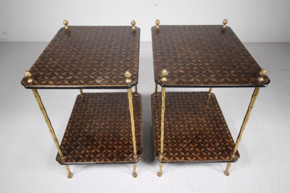 A pair of mid-century two-tier side tables with brass simulated bamboo legs and brown patterned lacquered surfaces topped with pinecone finials.