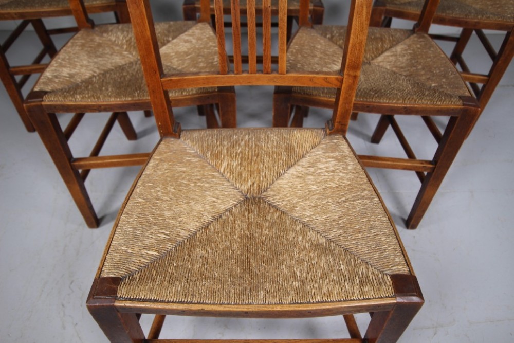 A set of six early 19th-century elm country dining chairs featuring vertical slat backs, turned bobbin top rails, and woven rush seats. View V