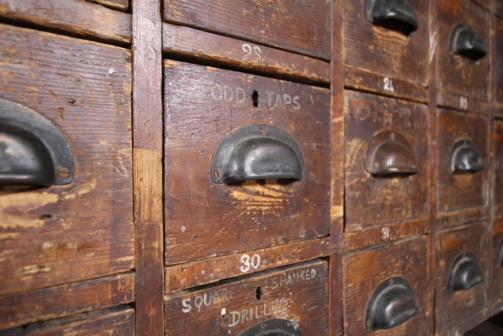 A large 19th-century pine bank of drawers featuring thirty-five small drawers with metal cup handles, top pigeonhole compartments, open bottom shelving, and a dark painted outer frame. View VI