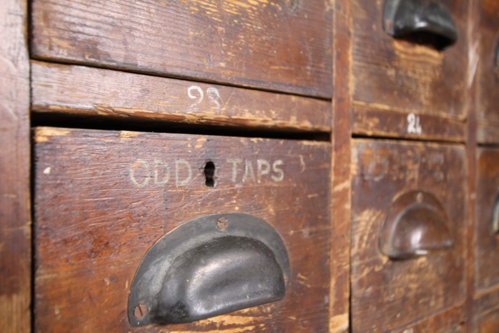 A large 19th-century pine bank of drawers featuring thirty-five small drawers with metal cup handles, top pigeonhole compartments, open bottom shelving, and a dark painted outer frame. View VII