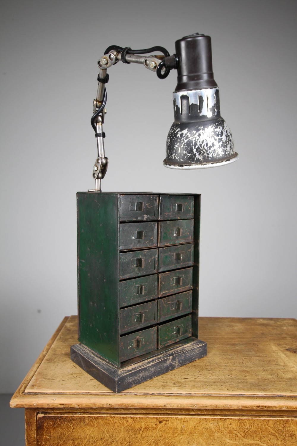 A dark green painted metal chest of twelve small drawers featuring an attached articulated industrial task lamp with a distressed shade. View II