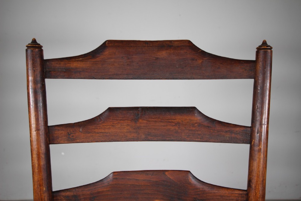 A nineteenth-century dark ash ladderback armchair featuring five horizontal back slats, sloped armrests, turned front legs, and a hand-woven rush seat. View V