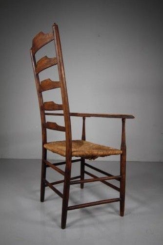 A nineteenth-century dark ash ladderback armchair featuring five horizontal back slats, sloped armrests, turned front legs, and a hand-woven rush seat. View II