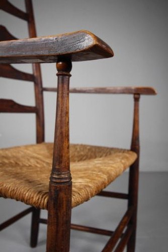 A nineteenth-century dark ash ladderback armchair featuring five horizontal back slats, sloped armrests, turned front legs, and a hand-woven rush seat. View VII
