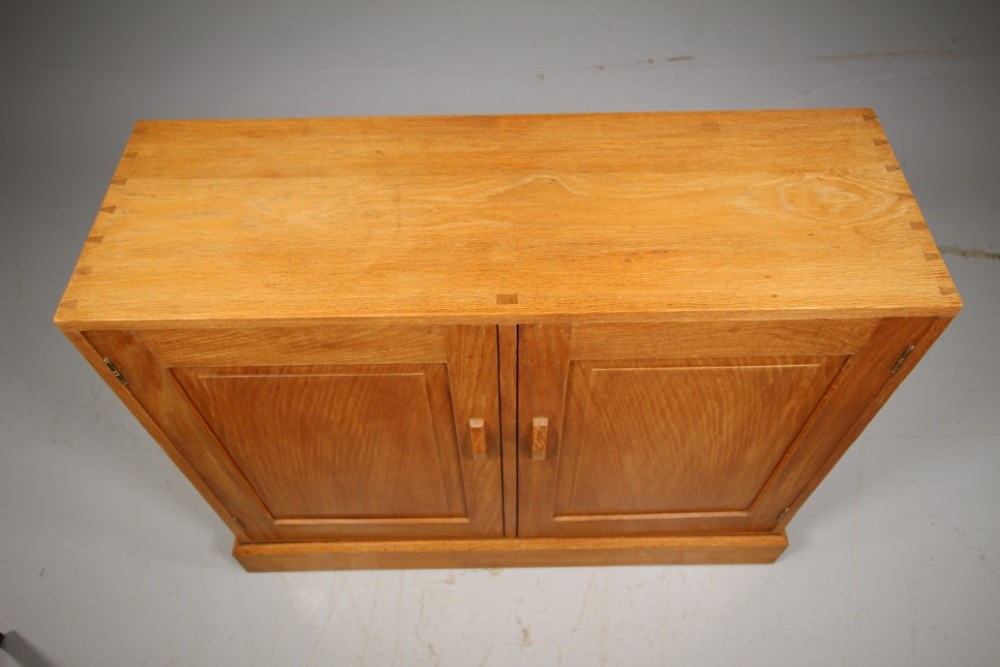 A 1930s English oak two-door cupboard featuring recessed panel doors, hand-carved wooden handles, and a solid plinth base. View II