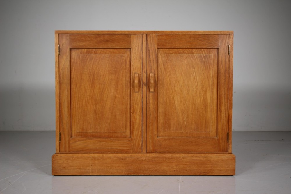 A 1930s English oak two-door cupboard featuring recessed panel doors, hand-carved wooden handles, and a solid plinth base. View III
