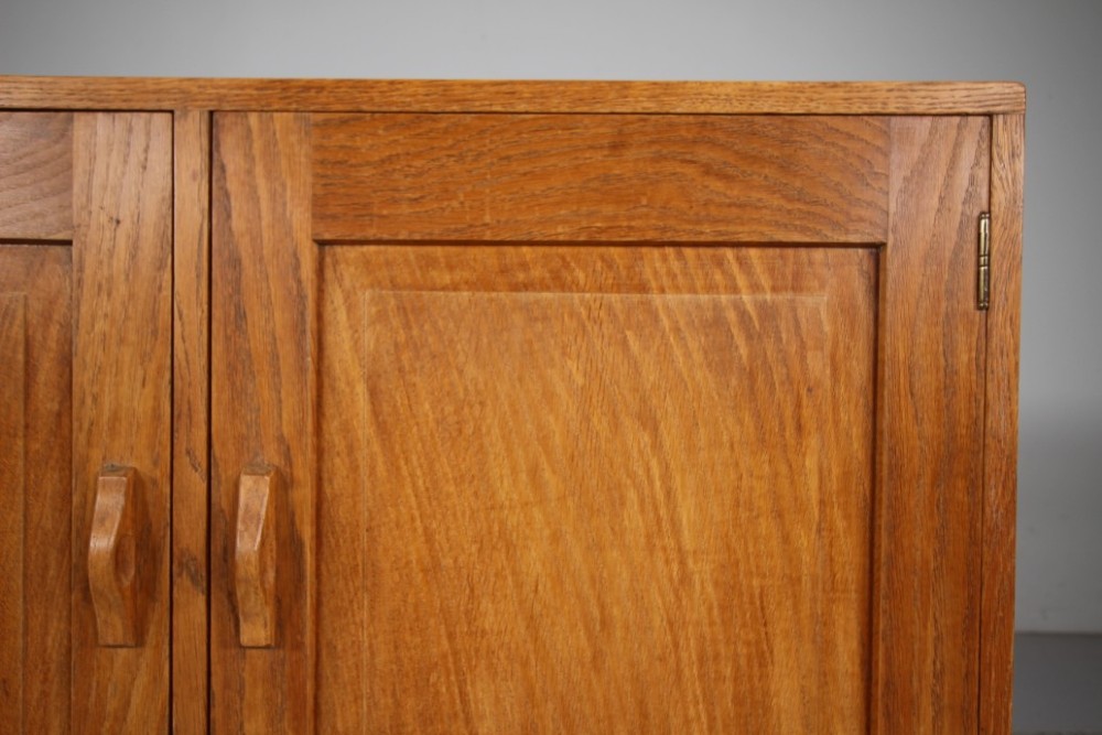 A 1930s English oak two-door cupboard featuring recessed panel doors, hand-carved wooden handles, and a solid plinth base. View IV