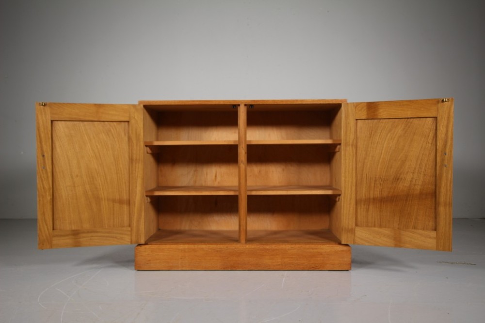 A 1930s English oak two-door cupboard featuring recessed panel doors, hand-carved wooden handles, and a solid plinth base. View V