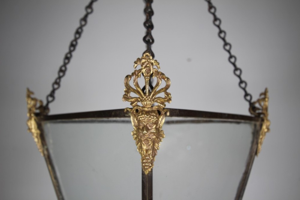 An 18th-century hanging hall lantern featuring a tapered clear glass body, dark bronze frame, detailed gilt bronze corner mounts, and suspension chains. View VIII