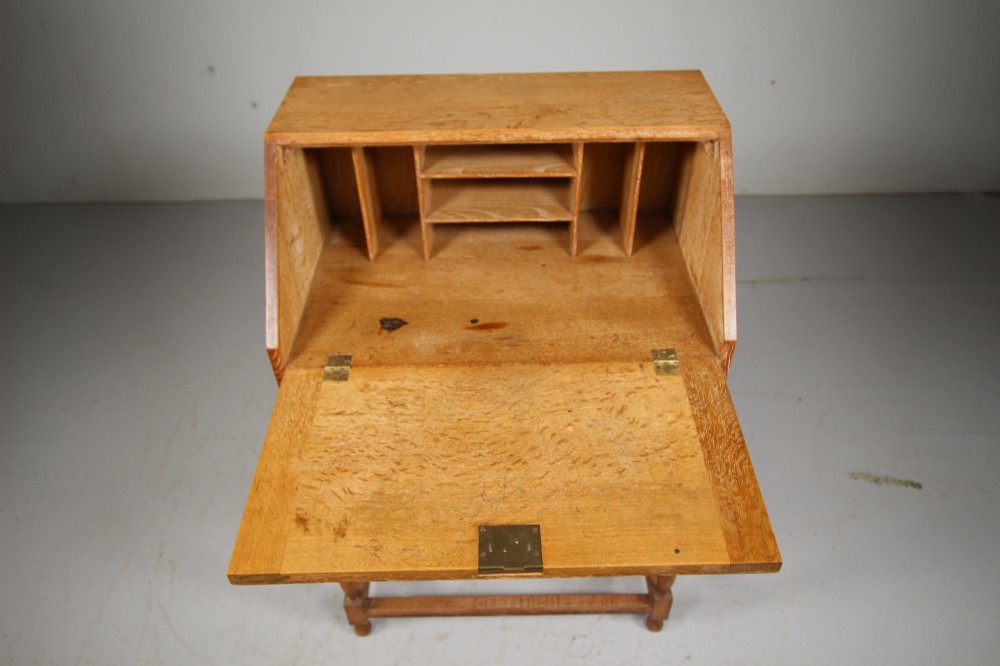 A 1920s light oak writing bureau featuring a slanted fall-front lid, two lower drawers with wooden knobs, and turned legs with a box stretcher. View VI