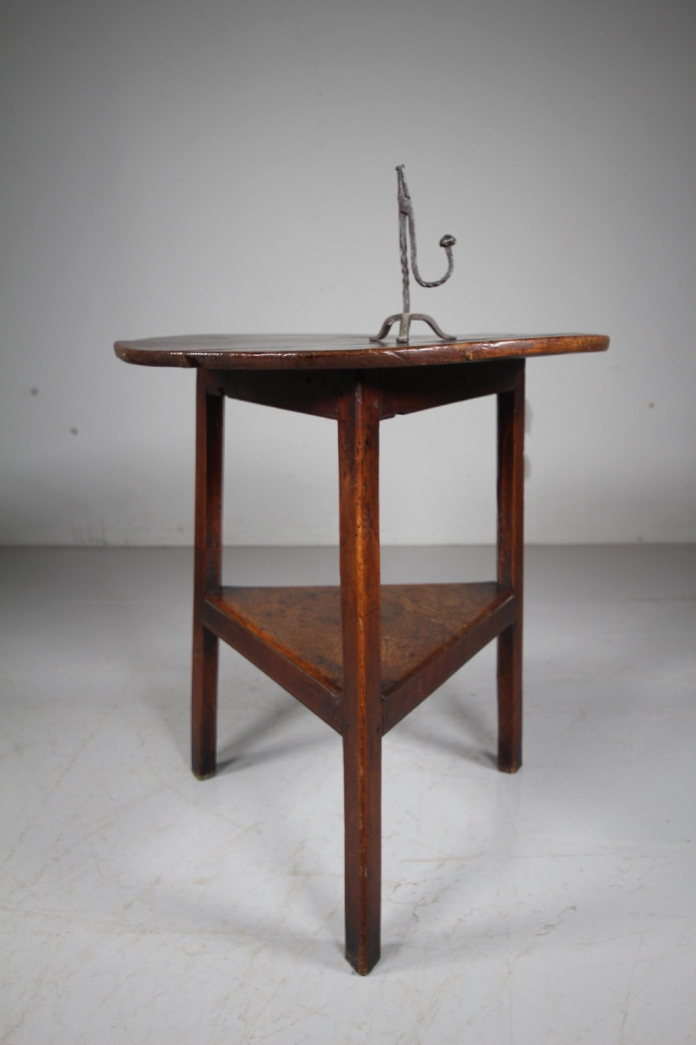 An English Georgian antique oak cricket table featuring three straight legs, a circular wooden top, and a lower triangular undertier shelf.