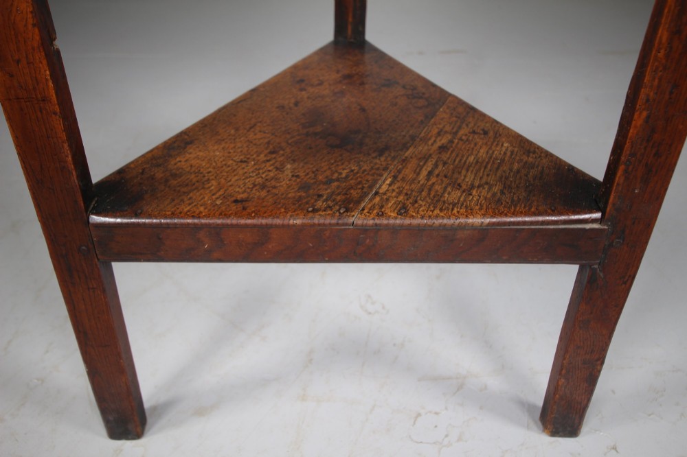 An English Georgian antique oak cricket table featuring three straight legs, a circular wooden top, and a lower triangular undertier shelf. View III