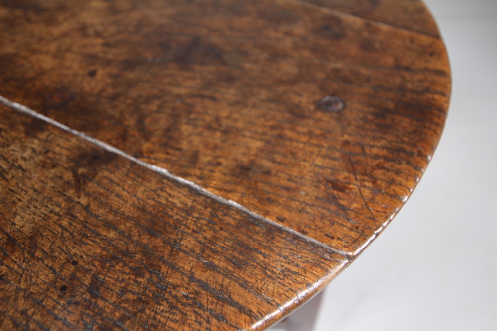 An English Georgian antique oak cricket table featuring three straight legs, a circular wooden top, and a lower triangular undertier shelf. View VI